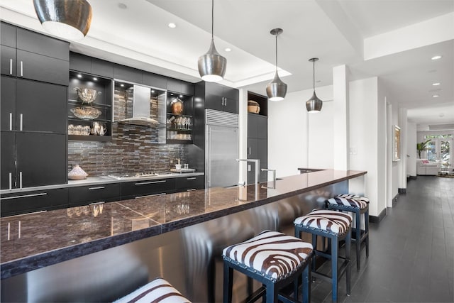 bar featuring pendant lighting, tasteful backsplash, wall chimney exhaust hood, stainless steel appliances, and dark hardwood / wood-style flooring