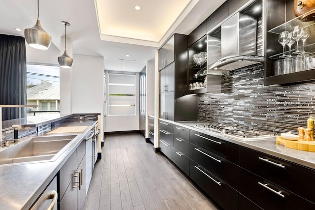 kitchen with wall chimney exhaust hood, wood-type flooring, backsplash, and decorative light fixtures