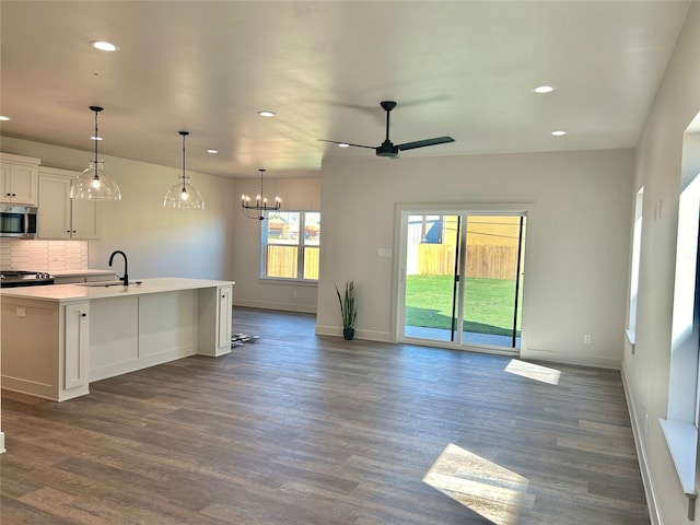 kitchen with tasteful backsplash, dark wood-type flooring, white cabinetry, a center island with sink, and decorative light fixtures