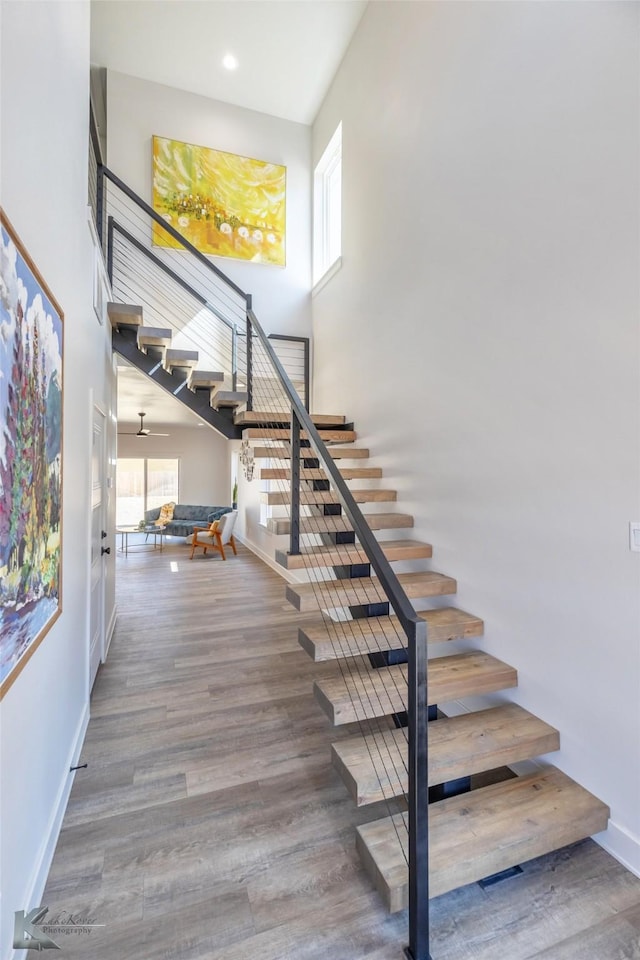 staircase featuring a high ceiling, recessed lighting, wood finished floors, and baseboards