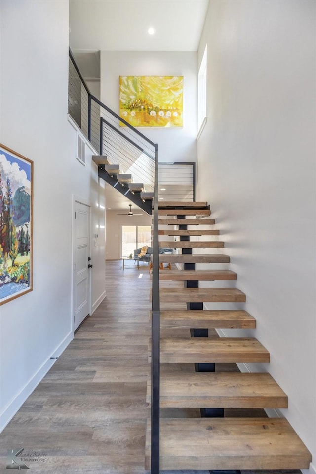 stairway featuring a high ceiling, wood finished floors, visible vents, and baseboards