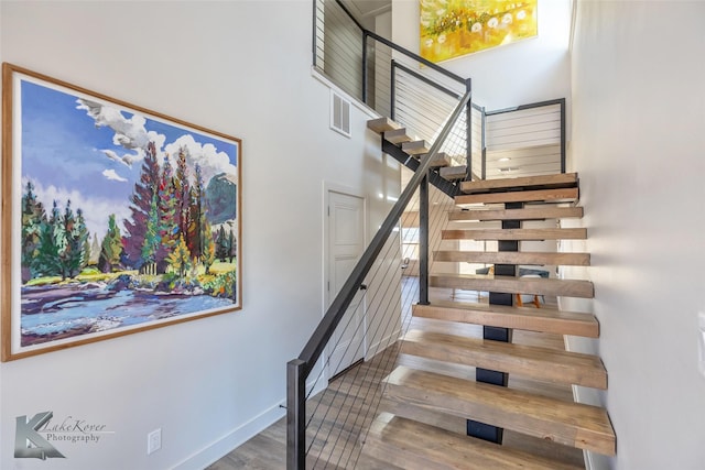 staircase with a high ceiling, baseboards, and wood finished floors