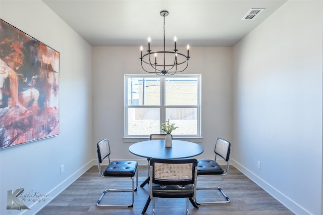 dining area with baseboards, wood finished floors, visible vents, and an inviting chandelier