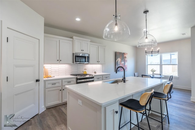 kitchen with stainless steel appliances, wood finished floors, a sink, decorative backsplash, and an island with sink