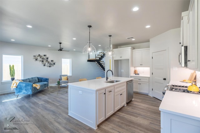 kitchen featuring stainless steel appliances, a sink, visible vents, white cabinets, and open floor plan