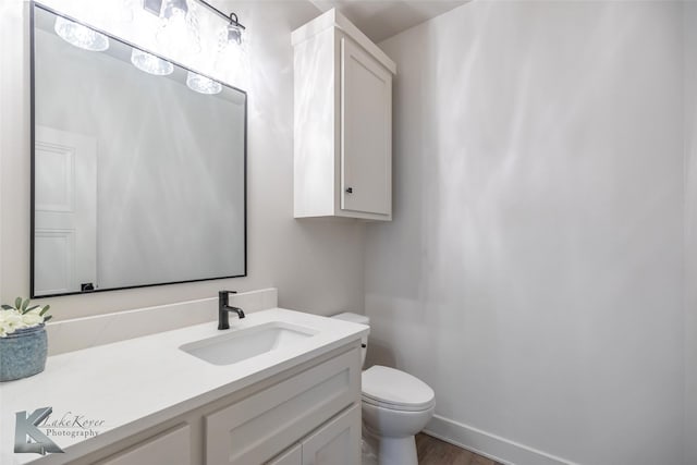 half bath with toilet, baseboards, wood finished floors, and vanity