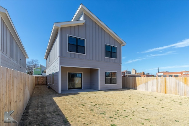 rear view of house with board and batten siding, a fenced backyard, and a patio