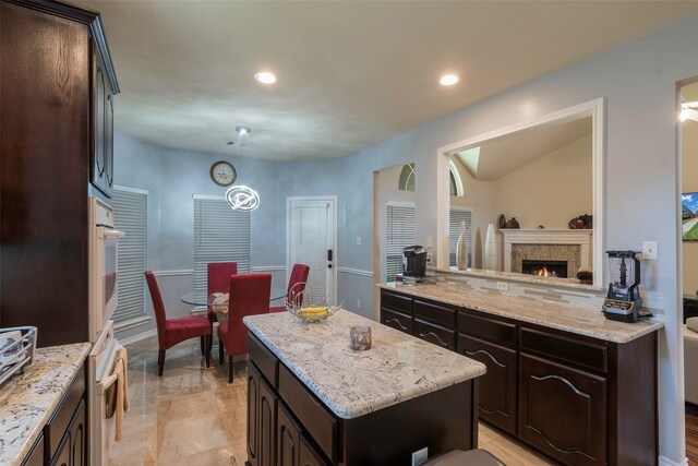 kitchen featuring tasteful backsplash, a kitchen island, dark brown cabinets, oven, and light stone countertops