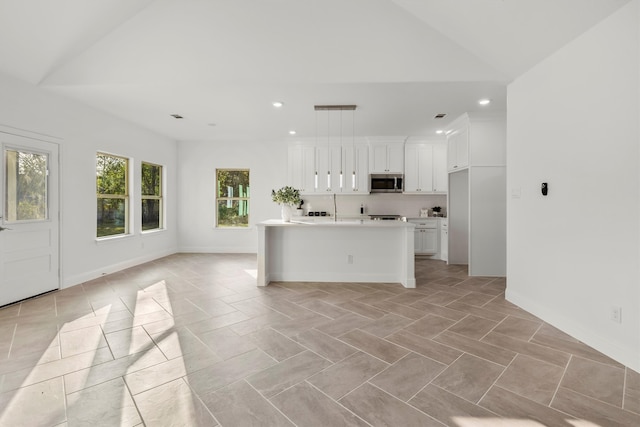 kitchen featuring lofted ceiling, decorative backsplash, an island with sink, hanging light fixtures, and white cabinetry