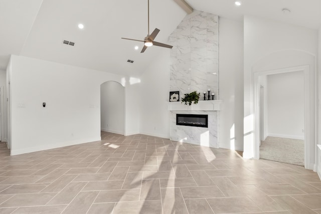 unfurnished living room with beam ceiling, high vaulted ceiling, a high end fireplace, and ceiling fan