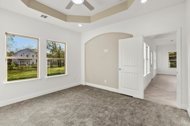 empty room featuring ceiling fan, carpet floors, and a raised ceiling