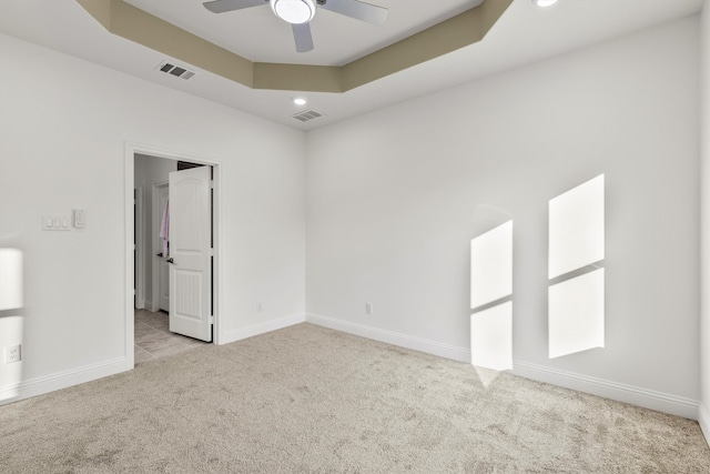 spare room featuring ceiling fan, a tray ceiling, and light colored carpet