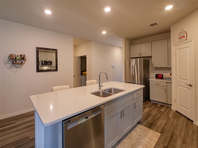 kitchen featuring gray cabinetry, dark wood-type flooring, a kitchen island with sink, sink, and stainless steel appliances