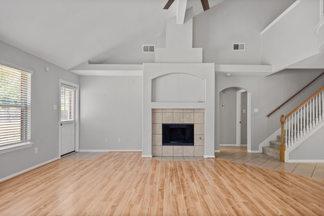 unfurnished living room with ceiling fan, light hardwood / wood-style flooring, a tiled fireplace, and high vaulted ceiling