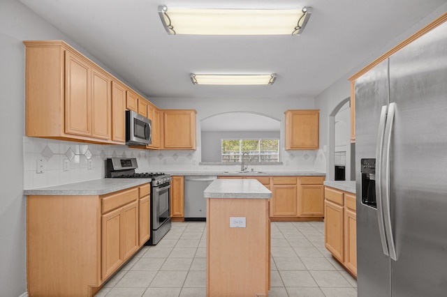 kitchen with appliances with stainless steel finishes, light tile patterned floors, light brown cabinetry, a center island, and sink