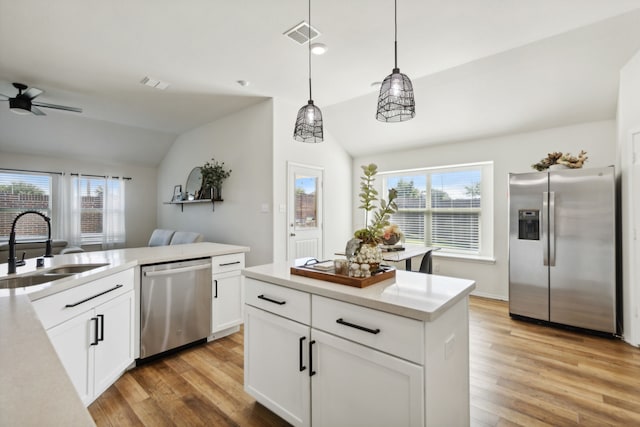 kitchen featuring light wood-type flooring, stainless steel appliances, vaulted ceiling, pendant lighting, and white cabinets