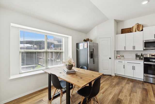 kitchen featuring light hardwood / wood-style flooring, vaulted ceiling, white cabinets, appliances with stainless steel finishes, and tasteful backsplash