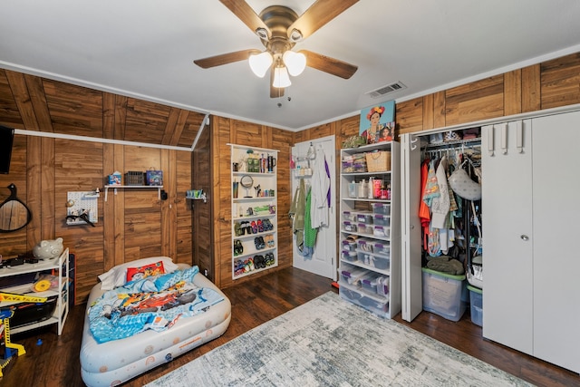 bedroom with ceiling fan, a closet, wood walls, and dark hardwood / wood-style floors