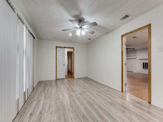 unfurnished bedroom featuring a brick fireplace, a closet, a textured ceiling, ceiling fan, and light hardwood / wood-style flooring