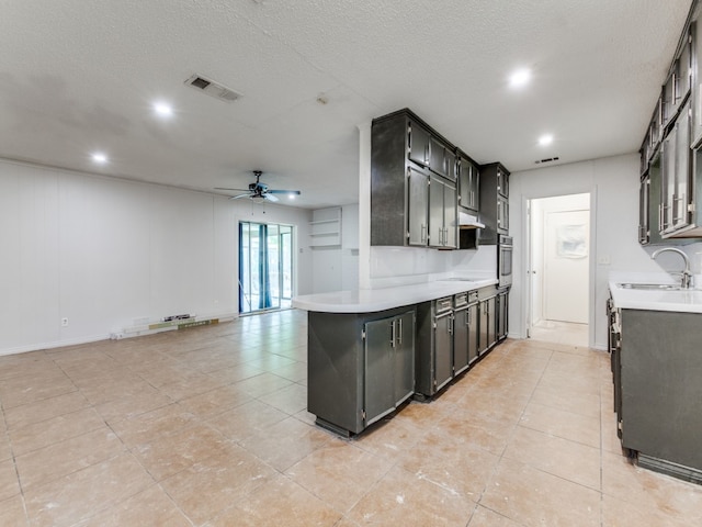 kitchen with a textured ceiling, sink, kitchen peninsula, oven, and ceiling fan