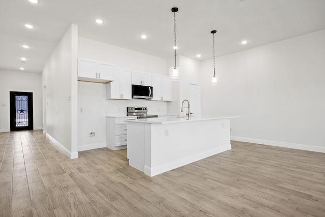 kitchen featuring light wood finished floors, a center island with sink, appliances with stainless steel finishes, white cabinets, and light countertops