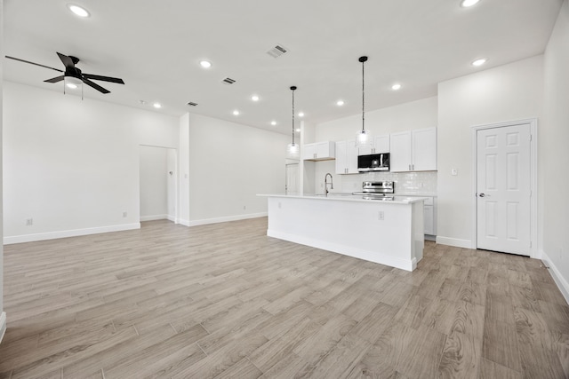 kitchen featuring a ceiling fan, a center island with sink, electric range, decorative backsplash, and open floor plan