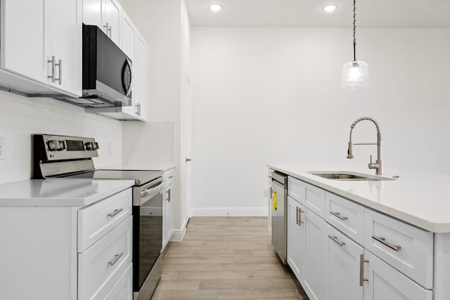 kitchen featuring light wood-style flooring, a sink, decorative backsplash, appliances with stainless steel finishes, and white cabinetry