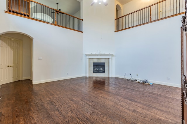 unfurnished living room featuring a high ceiling, dark wood-type flooring, ceiling fan, and a fireplace