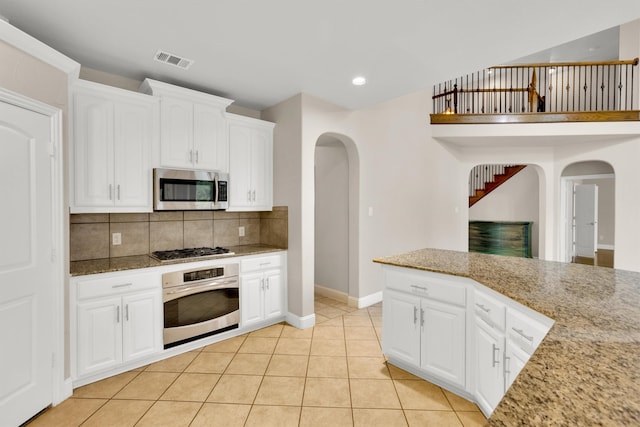 kitchen featuring white cabinetry, stainless steel appliances, backsplash, light tile patterned floors, and light stone countertops