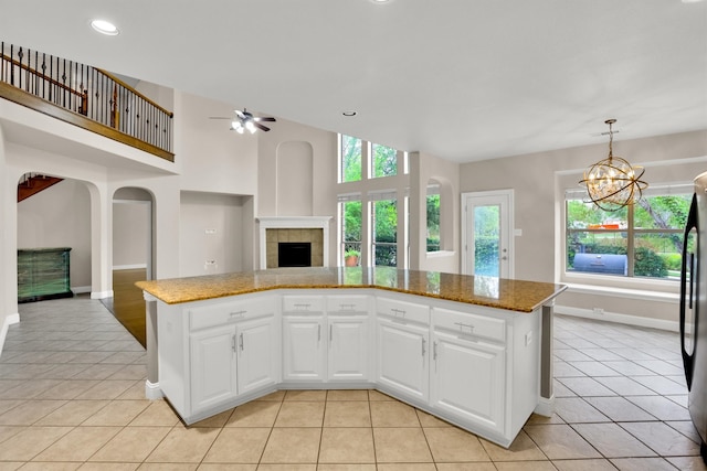 kitchen featuring ceiling fan with notable chandelier, white cabinetry, hanging light fixtures, and a fireplace