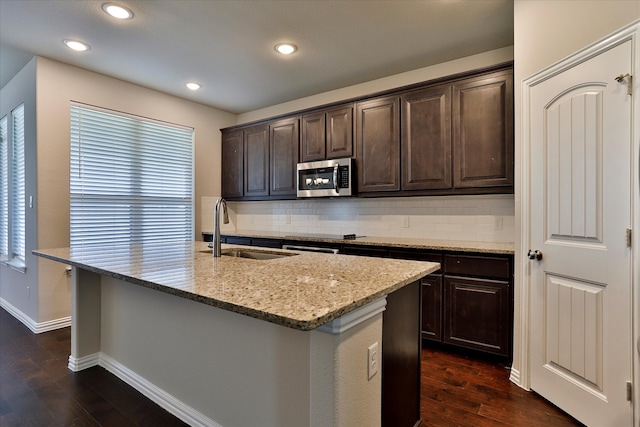 kitchen featuring a center island with sink, sink, dark brown cabinets, light stone counters, and dark hardwood / wood-style floors