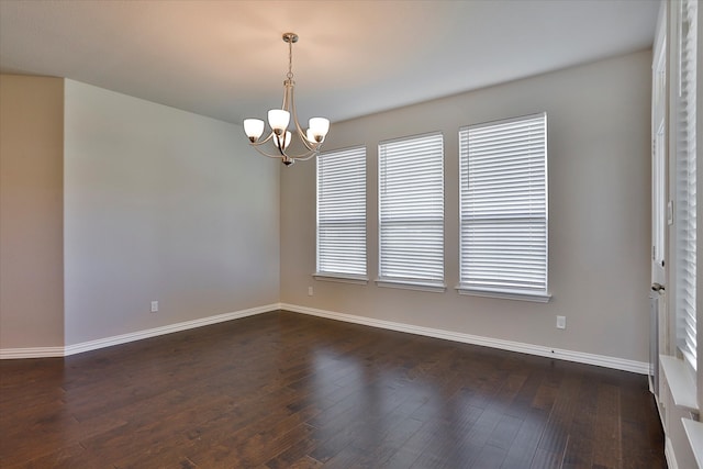 empty room featuring dark wood-type flooring and an inviting chandelier