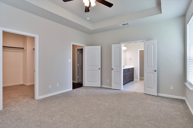 unfurnished bedroom featuring a spacious closet, ensuite bath, light colored carpet, and ceiling fan