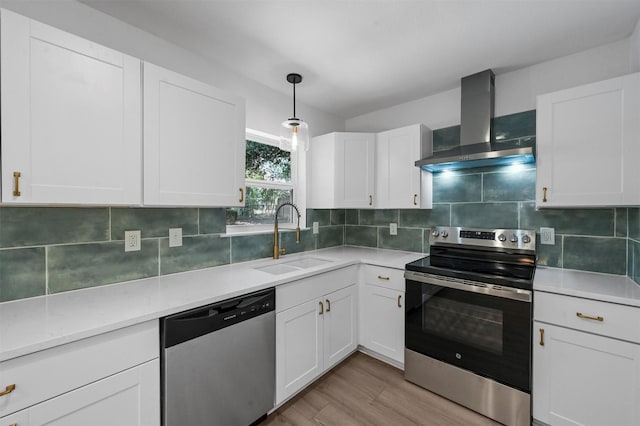 kitchen featuring pendant lighting, sink, appliances with stainless steel finishes, white cabinets, and wall chimney exhaust hood