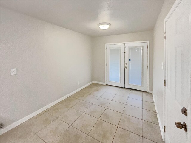 unfurnished room with light tile patterned flooring, baseboards, and french doors