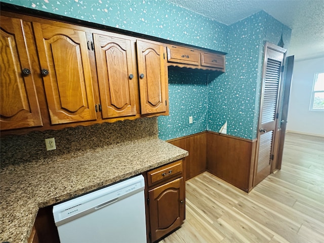 kitchen with white dishwasher, light stone countertops, light hardwood / wood-style floors, and a textured ceiling