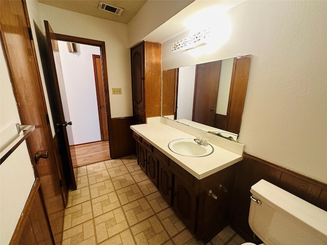 bathroom featuring vanity, wooden walls, and toilet