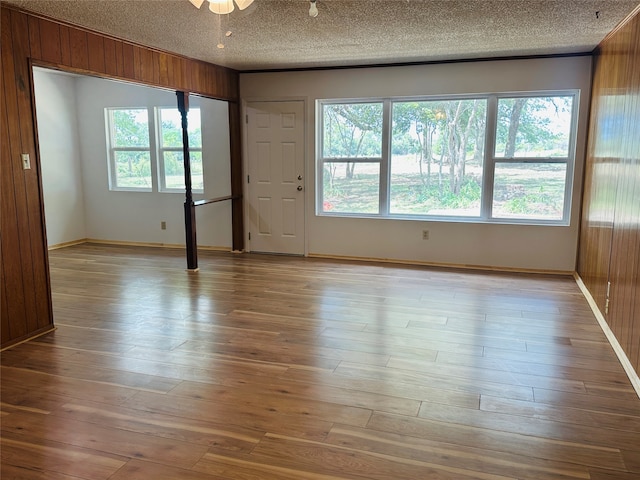 unfurnished room featuring light hardwood / wood-style floors, a textured ceiling, wood walls, and ceiling fan