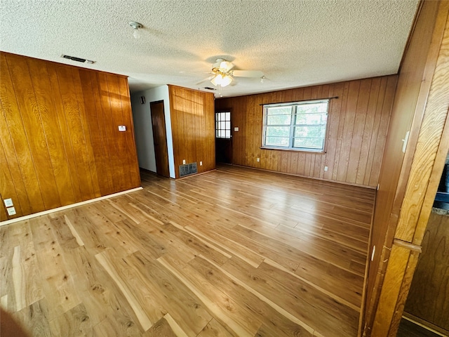 spare room with a textured ceiling, wood-type flooring, wooden walls, and ceiling fan