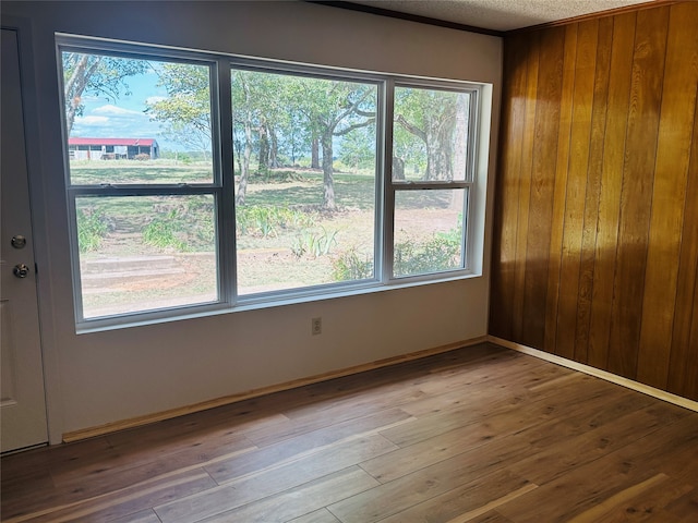 unfurnished room with wood-type flooring, a healthy amount of sunlight, and wooden walls