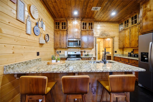 kitchen featuring a kitchen bar, wooden walls, appliances with stainless steel finishes, and sink