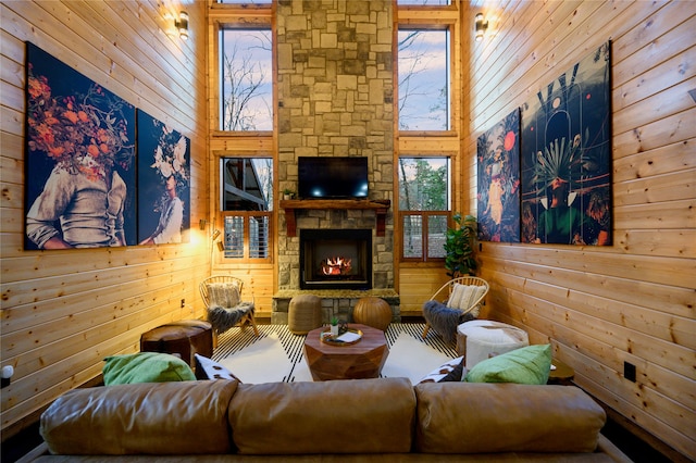 living room with a towering ceiling, wood walls, plenty of natural light, and a stone fireplace