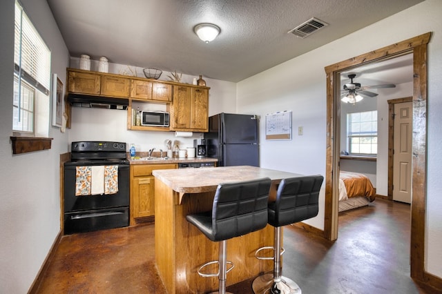 kitchen featuring a textured ceiling, a kitchen bar, a kitchen island, black appliances, and ceiling fan