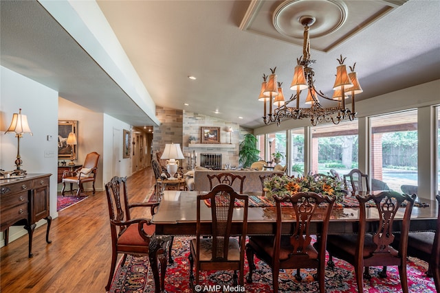 dining area featuring wood-type flooring, a chandelier, a textured ceiling, vaulted ceiling, and a fireplace