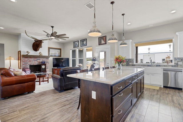 kitchen with stainless steel dishwasher, white cabinets, plenty of natural light, and a brick fireplace