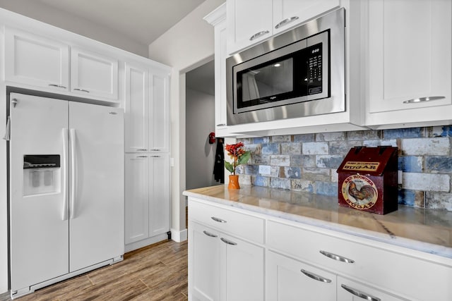 kitchen featuring decorative backsplash, white refrigerator with ice dispenser, white cabinets, stainless steel microwave, and light wood-type flooring