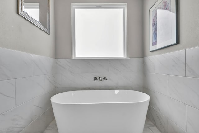 bathroom featuring a tub, tile walls, and a healthy amount of sunlight