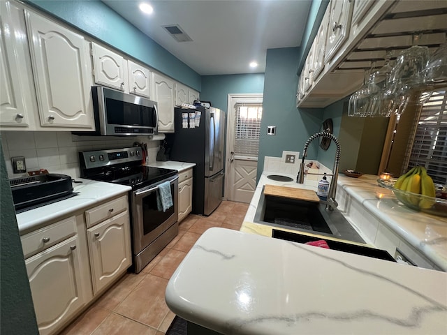 kitchen with appliances with stainless steel finishes, white cabinetry, sink, and light tile patterned floors