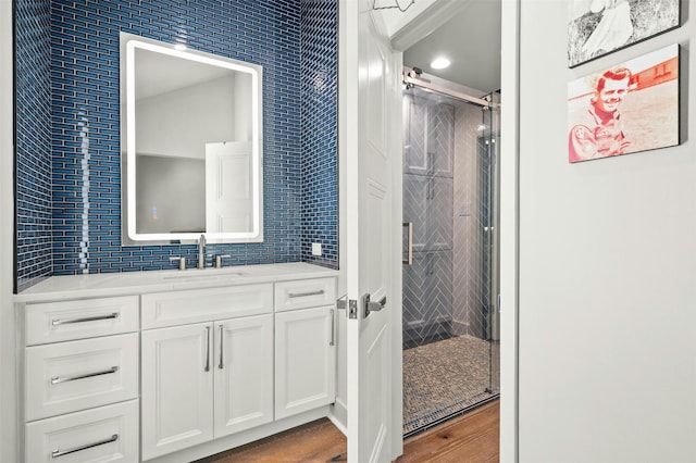 bathroom with backsplash, a shower with shower door, hardwood / wood-style flooring, and vanity