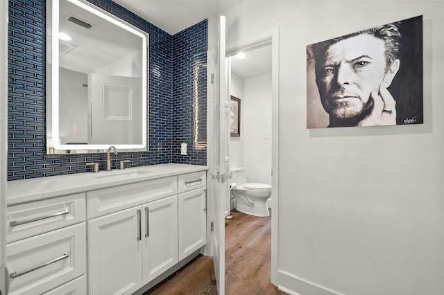 bathroom with decorative backsplash, hardwood / wood-style flooring, vanity, and toilet